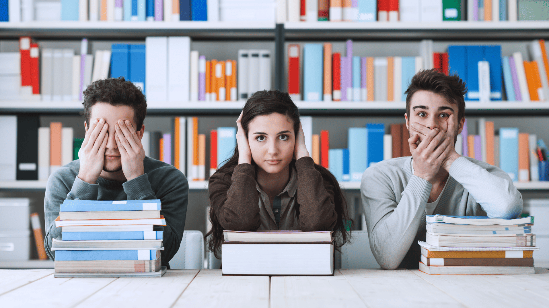 three people sitting in a library, one vovering their eyes, one covering their mouth, and one covering their ears
